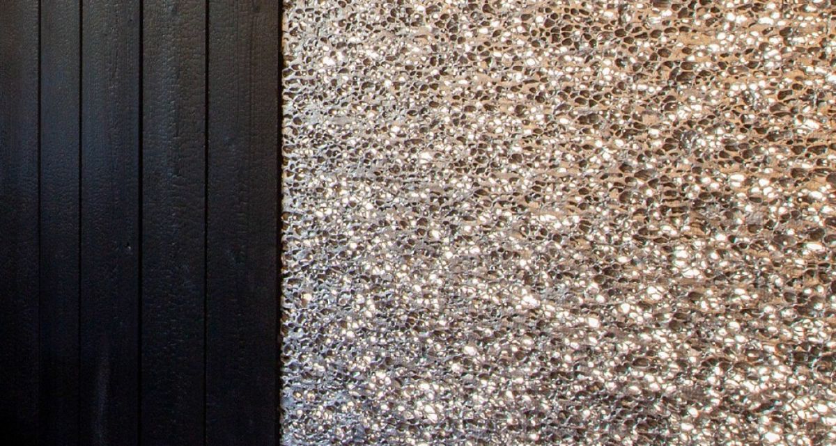 Eine feste Seitenwand an einer Überdachung auf der Terrasse aus verbrannten Holz und aufgeschäumtem Aluminiumschaum Wand.